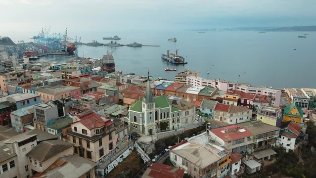Aerial dolly in of colorful houses and Lutheran Church leading to Valparaiso Sea Port and ships docked, Chile