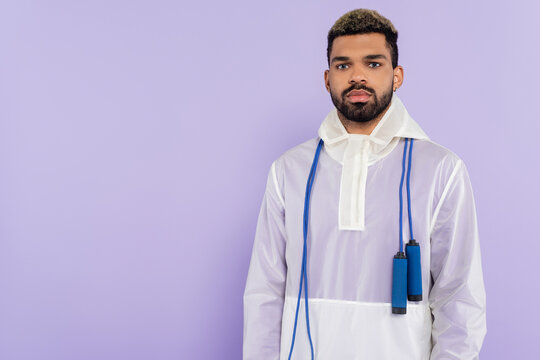 young african american man in trendy sportswear with skipping rope isolated on purple.