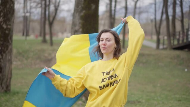 The girl walks in the park with the flag of Ukraine. Ukrainka is happy for Ukraine. Ukrainian national symbols.