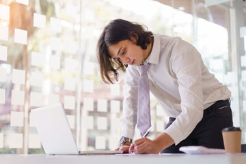 Business concept, Businessman writing down ideas in notebook and checking information on laptop