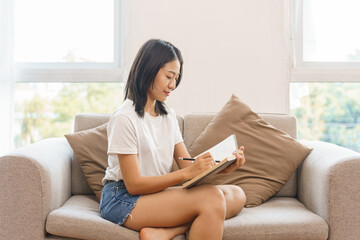 Home relaxation concept, Young woman sitting on couch to taking notes on notebook at home