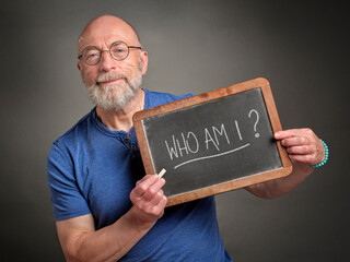 Who am I? Senior man is sharing inspirational question handwritten on a blackboard. Philosophy, identity and personal development concept.