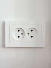 Electric socket for two pins of white color on a light wall, close-up