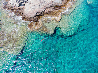 Unrecognizable woman swimming on azure water texture, transparent sea surface with a rocky bottom....