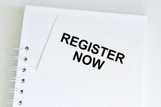 Register Now inscription on a white card on a notebook on a table, a business concept