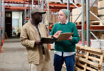 Fototapeta na wymiar Female warehouse worker discussing list with delivery man while they standing in storage room