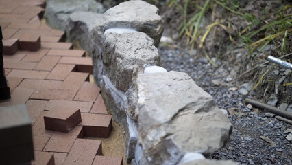 Closeup of brick paver going into place along a rock wall edge in hardscaping landscaping patio project.