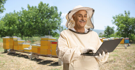 Bee keeper in a uniform working on a computer on apiary