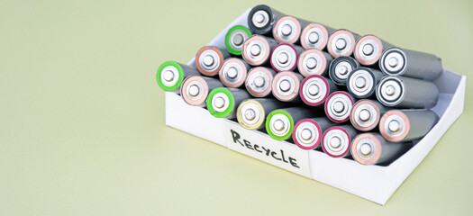 Used AA batteries and proper disposal of environmentally and soil toxic batteries on a green background.
