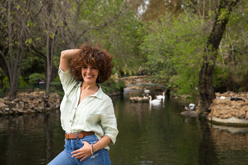 beautiful woman with curly hair is standing in front of a pond of ducks and swans in the park. The woman is on holiday in Seville and enjoys the scenery and the holiday. Holiday and travel concept.