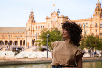 Obraz premium beautiful woman with curly hair is on holiday in sevilla. The woman is posing for pictures in front of the most famous square of the centuries old city. Holiday and travel concept.
