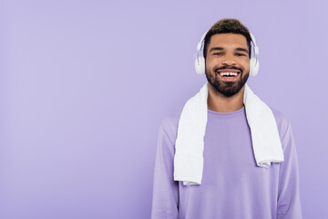 bearded and happy african american man in wireless headphones isolated on purple.