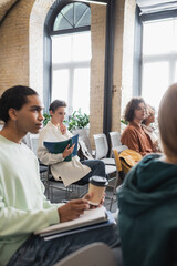 blurred african american man holding coffee to go while sitting in classroom with interracial students.