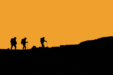 Fototapeta na wymiar Silhouette escursionisti che camminano in montagna con cielo arancio 