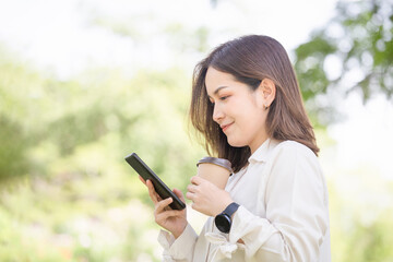 Portrait of Young woman using smartphone and holding drinks takeaway coffee while standing in the garden