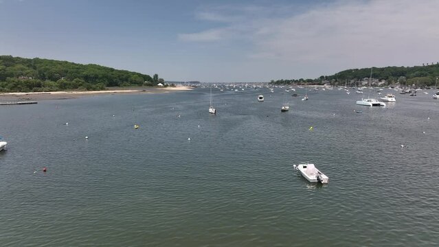 An aerial view of the Northport Marina on Long island, NY with many anchored boats. It is a sunny day with blue skies and white clouds above. The camera dolly in and boom up over the sailboats.