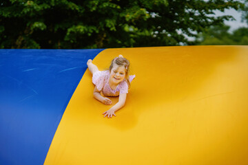 Little preschool girl jumping on trampoline. Happy funny toddler child having fun with outdoor...