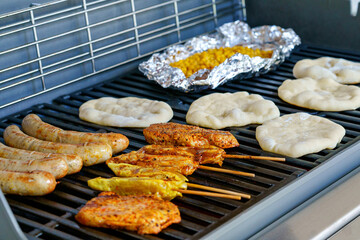 Assorted meat grilling over the hot fire on a portable barbecue with steak, sausage, kebabs, chicken , spare ribs and corn and bread.