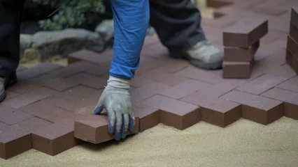 Crédence de cuisine en verre imprimé Chocolat brun Hand putting red brick pavers into place in a herringbone pattern on a bed of sand in hardscaping landscaping patio project.