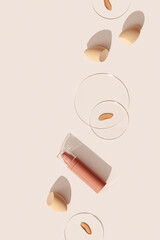 Bottle of makeup foundation cream, samples on glass disk, beauty blender sponge on beige color background with hard light. Skin care beauty product. Top view package concealer base container