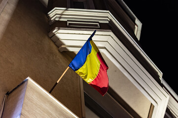 Romanian flag waving in wind hanging by the exterior side of a public building