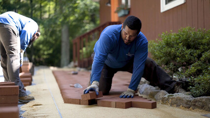 Man putting brick pavers into place in a herringbone pattern in a hardscaping, landscaping patio...