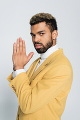 young african american man in pastel yellow blazer with praying hands isolated on grey.