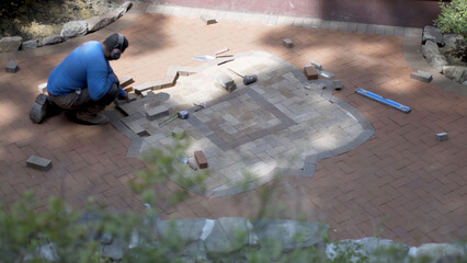 Wide shot of man fitting brick pavers into a custom designed two tone hardscaping emblem.