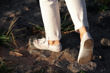 Legs of  woman in white shoes walking on sand