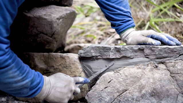Closeup of putting mortar between large stones in a rock wall design in hardscaping landscaping project.
