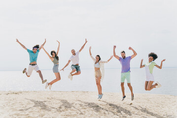 Full size portrait of active cheerful buddies rejoice jumping sand beach water sea outdoors