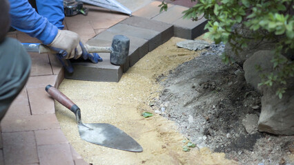 Man using a rubber mallet to tap a brick paver into place along a rock edge of a garden.