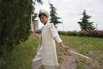 Turkish boy wearing traditional clothing during a circumcision ceremony. Boy standing outdoors among trees.