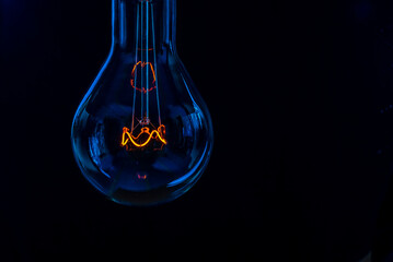 Glowing lamp, tungsten light bulb lit on black background,  close up shot, on wood table,  idea concept,  natural wax candle, Burning candle near a switched off light bulb in complete darkness.