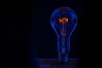 Glowing lamp, tungsten light bulb lit on black background,  close up shot, on wood table,  idea...