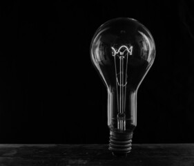 Glowing lamp, tungsten light bulb lit on black background,  close up shot, on wood table,  idea...