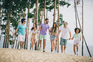 Full length portrait of friendly overjoyed people hold arms running sand beach hanging out outdoors