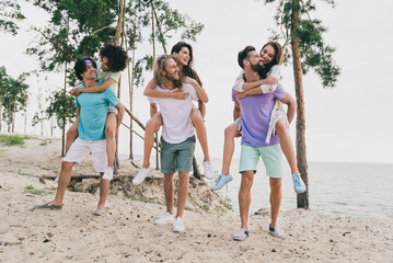 Photo of charming funny people group holding girls arms having fun enjoying good weather outside ocean water