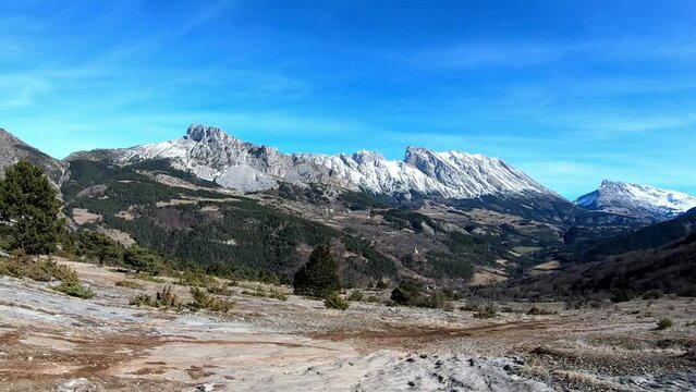 Panoramic view of snowy mountains, forests and rocks on a blue sky with some clouds in Devoluy. high point of view.french alps winter 2022