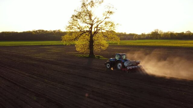 Aerial view of blue tractor at work in spring field. Preparation time of sowing. Shooting from drone flying over tractor in field with prepared soil for planting. Agriculture concept. Rural landscape.