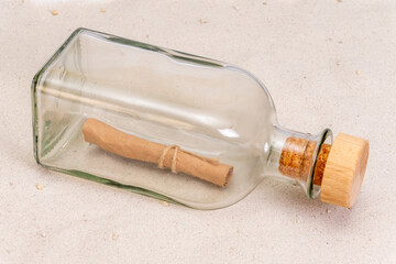 A rolled-up old paper note in a glass bottle with a cork on a light background. Concept: sea mail,...