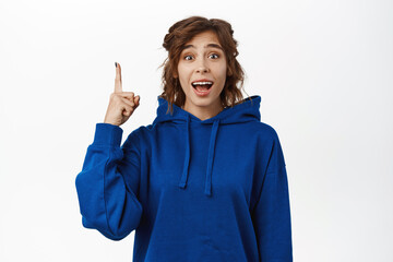 Happy young woman pointing finger up, showing advertisement, realise smth awesome, sharing information, making announcement, standing over white background