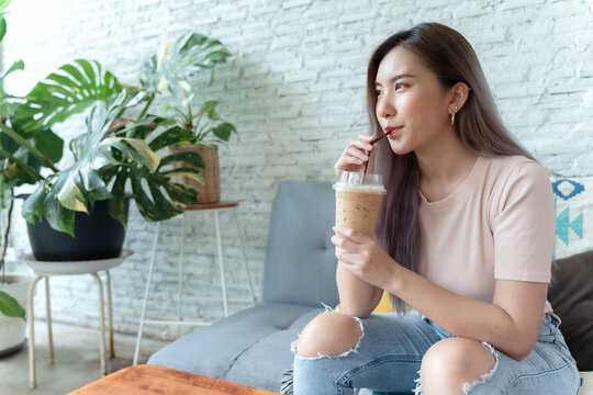 Asian woman sitting and drinking iced coffee and smiling happily.