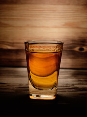 Shot glass of aged whiskey, close-up on a wooden table and against a background of a wooden unfocused texture
