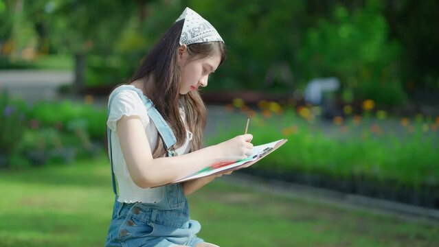 Portrait of attractive young pretty girl sitting in the public garden and drawing or painting a picture in summer season. Inspiration in green spring park. Art and relaxation on the holiday