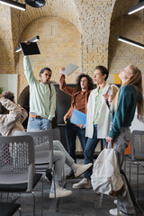 excited multiethnic students with closed eyes showing win gesture in auditorium.