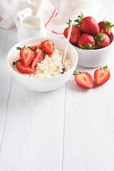 Cottage cheese with strawberries. Breakfast from cottage cheese with slices fresh strawberries, cream, cup of coffee in white bowl on white wooden background. Top view. Food concept. Mock up.