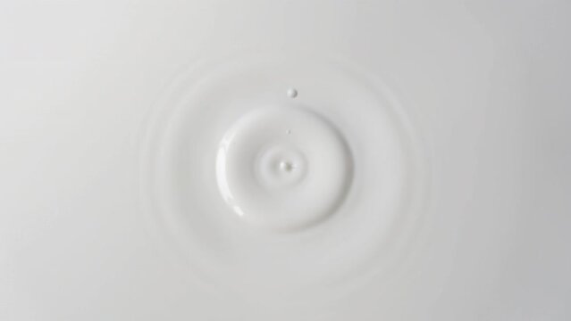 Drops of milk drip from top to center on a solid surface of milk close-up. Background of milk with falling drops. 4k raw slow motion video. Filmed on high speed cinema camera, 1000fps.