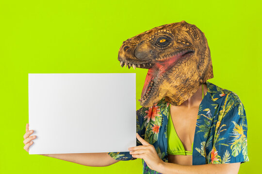 Funny woman wearing dinosaur animal mask holding blank empty white cardboard isolated on green studio background