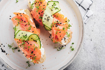 Sandwiches. Salmon toast with cream cheese, cucumber, black sesame and microgreens on gray concrete table background. Seafood. Healthy food. Top view.